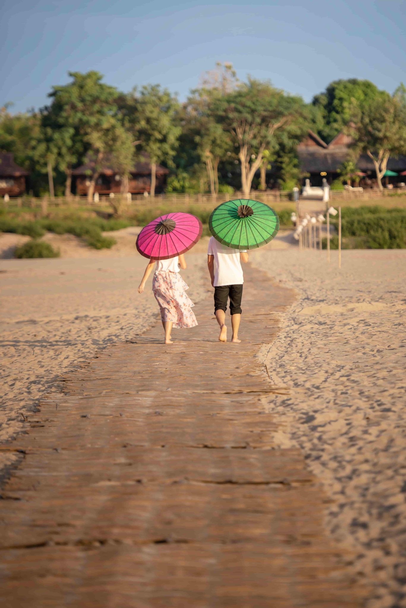 Two walkers carry colourful parasols across the open sand.