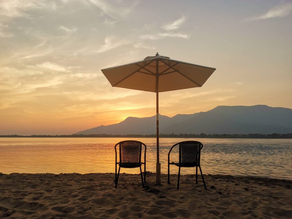 Two chairs beneath a parasol, facing the evening river.