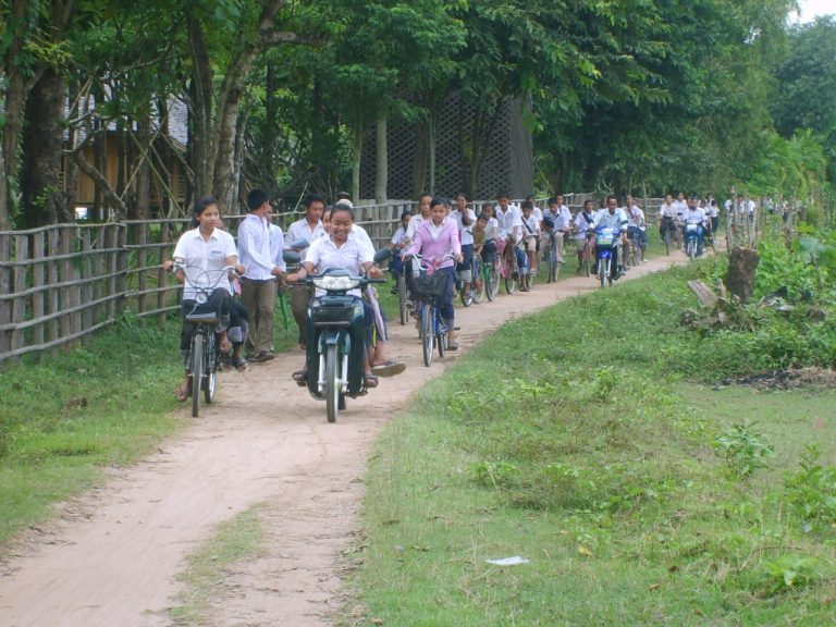 A group of cyclists follows a path through the village.