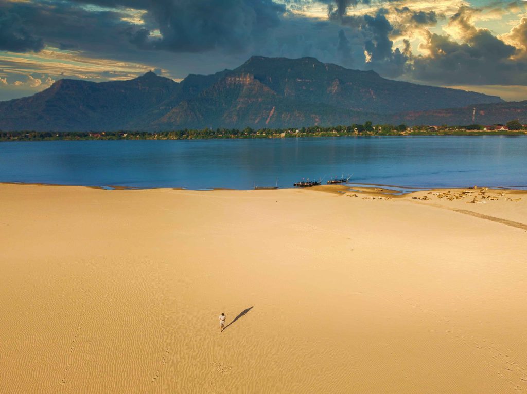 Open sand, blue water and mountains across the river.
