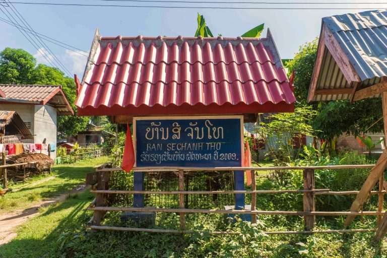 A village entrance sign beneath its red roof.