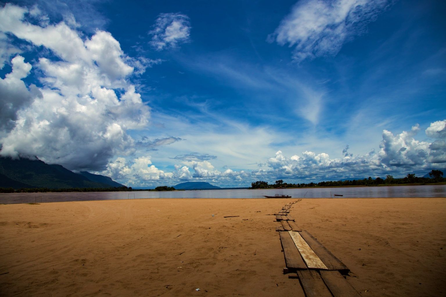A narrow walkway crosses the broad sandbank towards the Mekong.