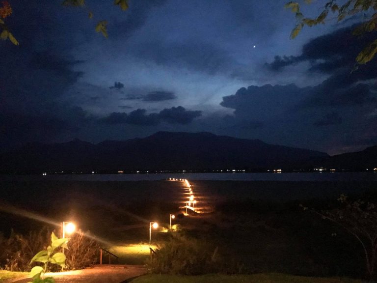 Small lights trace the sandy riverbank after dark.